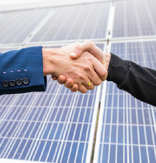 Two individuals shaking hands in front of solar panels