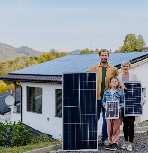 Family standing in front of their house, holding solar panels