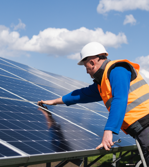 A man in an orange safety vest and hard hat is actively working on a solar panel installation project